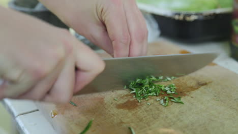 person using sharp chef knife to cut pieces of rosemary leaves for cooking