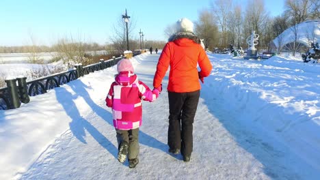 Back-view-mother-and-daughter-running-in-winter-park.-Happy-wintertime