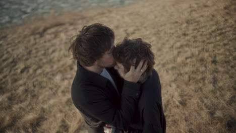 overhead view of couple sharing forehead kiss on dry grass lakeshore