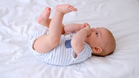 Cute-little-baby-chewing-his-hands-lying-on-bed-in-the-bedroom-4k