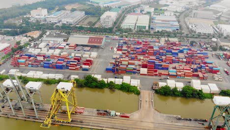 stacked containers at river port, drone tilt-down reveals port cranes, saigon