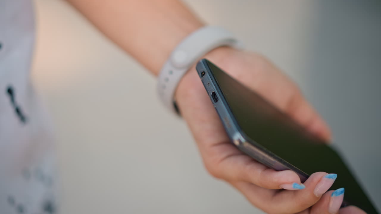 Closeup caucasian woman hands holding smartphone during quiet morning routine, plugging white earbuds into phone jack, fitness wristband visible, soft natural light, shallow depth of field, gentle