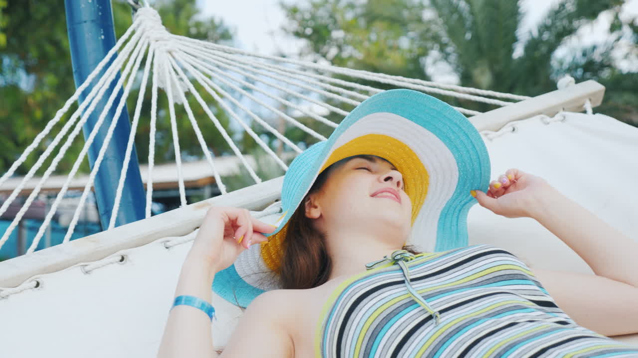 리조트 호텔에 있는 흰색 해먹에 챙이 넓은 모자를 쓴 검은 머리 소녀의 초상화