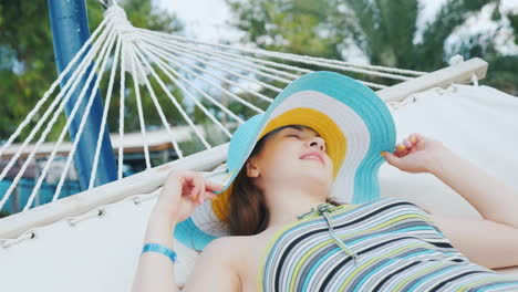 portrait of a young dark-haired girl in a broad-brimmed hat on a white hammock at the resort hotel