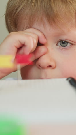 little boy looks through imaginary sight at pins with flags in notebook at table closeup. curious child learns location tags in copybook at lesson