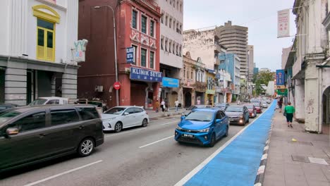 busy street lined with urban buildings, hotels, cafes, shops, with car and motorbike traffic in little india in capital city of kuala lumpur, malaysia