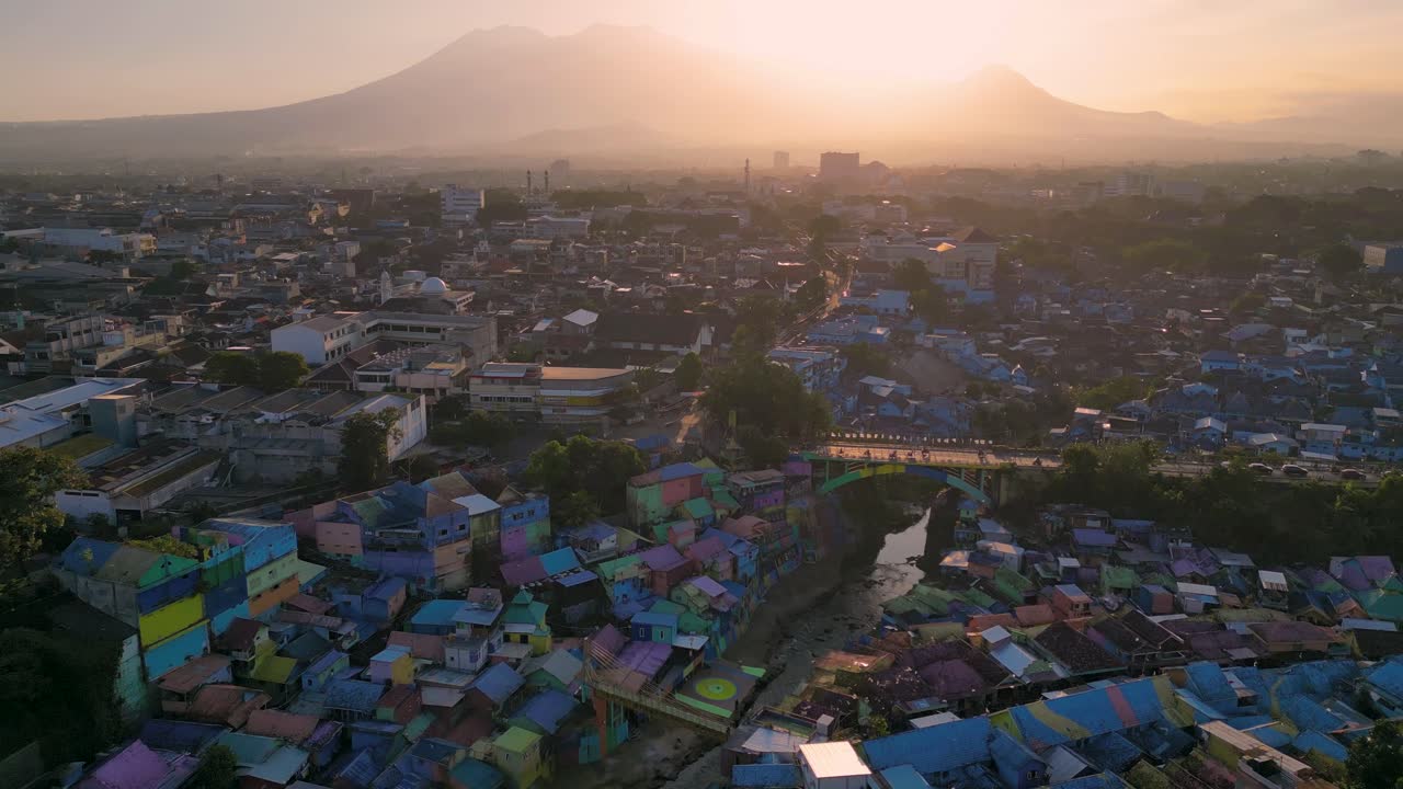 Pemandangan udara matahari terbenam oranye yang bersinar di desa Pelangi dan desa Biru dengan Gunung Berapi di latar belakang di Malang, Jawa Timur - Indonesia.