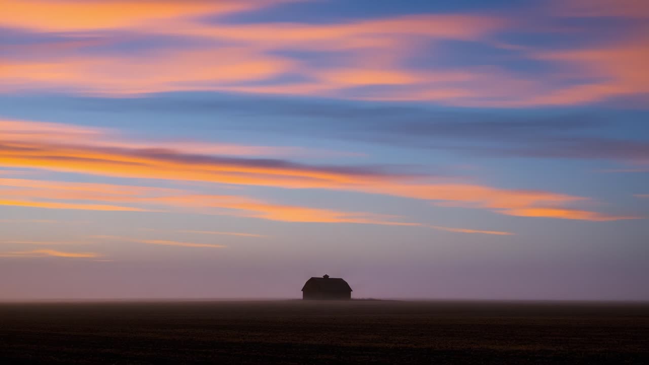 A solitary house stands in the heart of a vast landscape, illuminated by the evolving colors of dawn and dusk, enveloped in a mystical fog that creates a captivating atmosphere