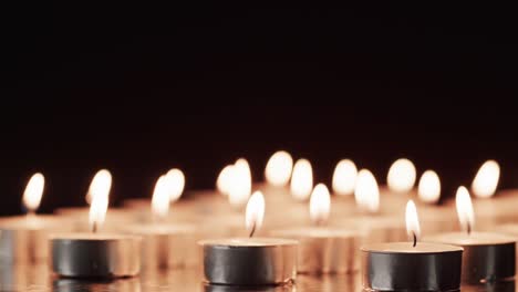 video of rows of tea candles with white flames and copy space on black background