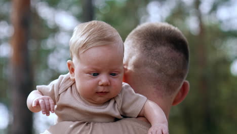 little blond baby boy on dad's shoulder. cute infant portrait close up. mom's hand touches kid's nose.