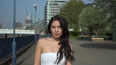 Attractive-and-playful-hispanic-latina-woman-walking-towards-the-camera,-on-the-riverbank-of-the-Thames-in-London,-UK