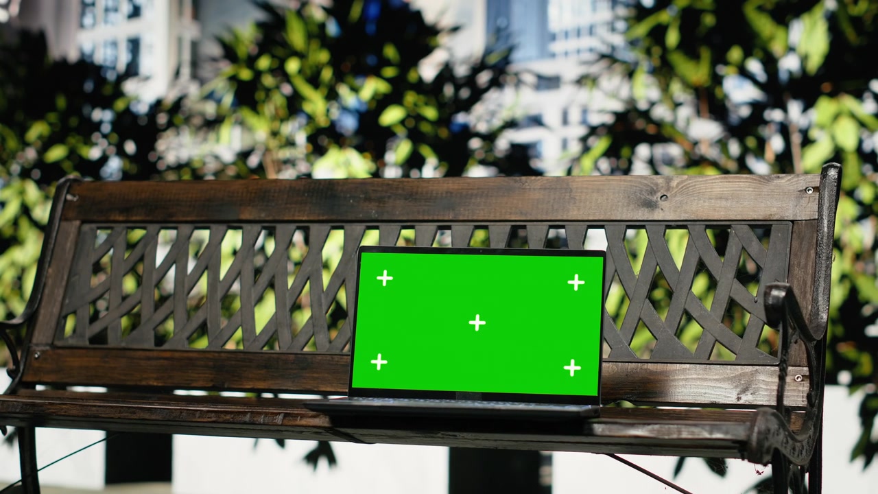 Laptop con schermo verde su una panchina di legno in un parco urbano