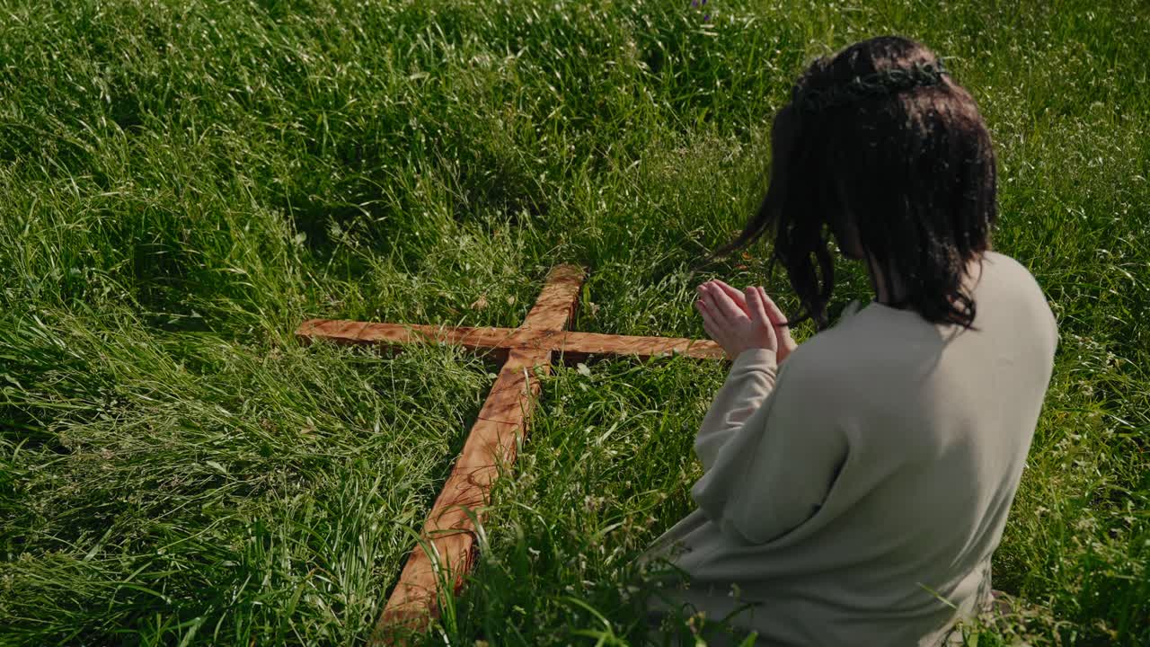 Jezus klęczący w trawie, trzymający drewniany krzyż, symbolizujący ukrzyżowanie i Pasję Wielkanocną.