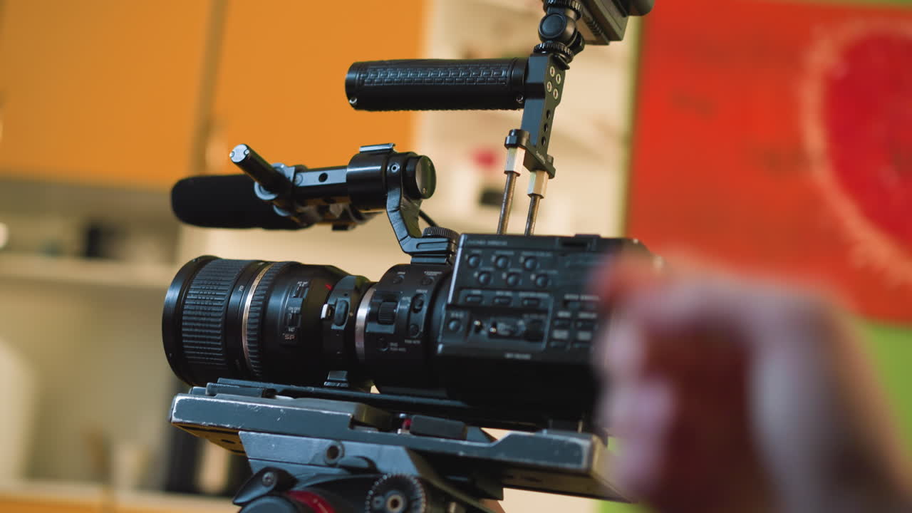 cameraman adjusting camera on tripod, focusing lens and hand positioning for filming in studio setup, preparing equipment for professional shot during video production in controlled workspace