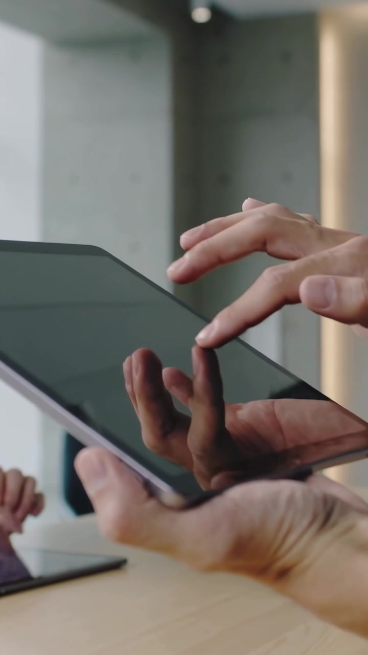 Vertical video: Reaching user starting taps, holder holding tablet at meeting table for demo