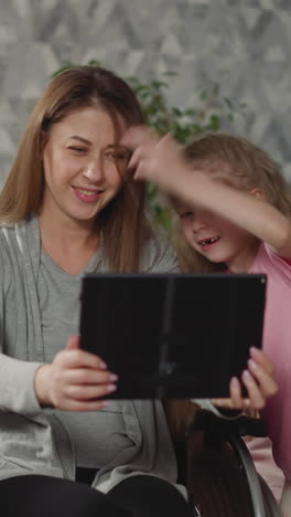 happy mother takes selfies with active kids on modern tablet making funny facial expressions. woman in wheelchair enjoys having fun with children