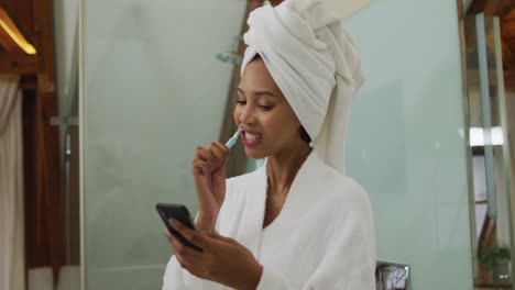 mixed race woman brushing teeth using smartphone