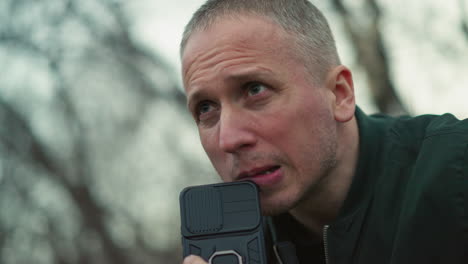 a close view of a concerned man looking intensely at something off-camera, holding a black smartphone near his mouth