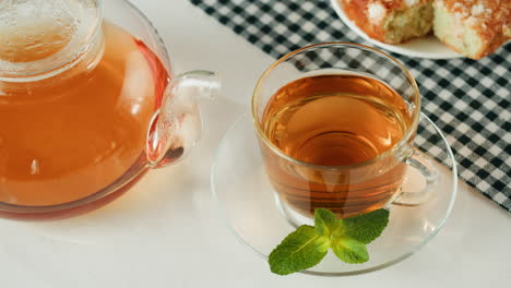 glass teapot and cup with mint and pastry
