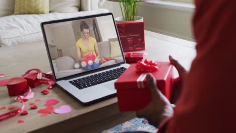 Fröhliche-Gemischtrassige-Frau,-Die-Ein-Geschenk-öffnet-Und-Einen-Videoanruf-Zum-Valentinstag-Auf-Dem-Laptop-Tätigt