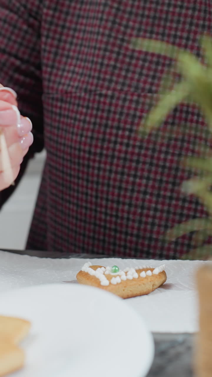 primer plano de una vela roja en llamas con una bandeja de galletas y una flor decorativa mientras la mujer usa una bolsa de tubería para aplicar detalles intrincados de hielo en la galleta