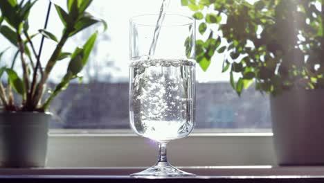 Man's-hand-is-holding-bottle,-while-pouring-pure-water-to-transparent-glass