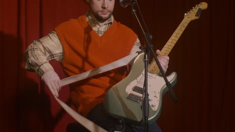 concentrated male musician with guitar and microphone sitting on stool and getting ready for a live performance