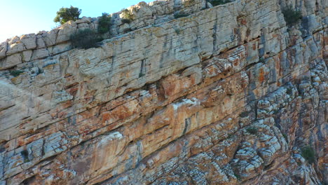 Vista-Aérea-De-Una-Enorme-Pared-Rocosa-En-Un-ángulo-Que-Se-Mueve-Hacia-Arriba-Y-Hacia-La-Derecha,-Mostrando-La-Erosión-Natural-De-La-Roca