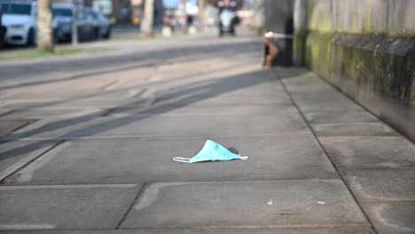 Person-walking-past-a-discarded-used-face-mask-on-the-sidewalk-on-a-sunny-day