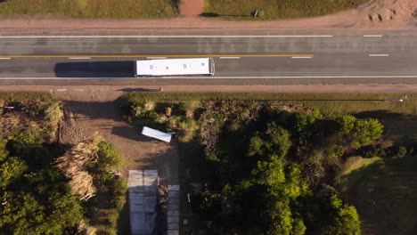 Drone-Aéreo-Que-Asciende-Vista-De-Arriba-Hacia-Abajo-De-La-Persona-Que-Se-Baja-Del-Autobús-Blanco-En-La-Parada-De-Autobús-Y-Cruza-La-Carretera-Principal-De-La-Zona-Residencial-De-El-Chorro-En-Uruguay