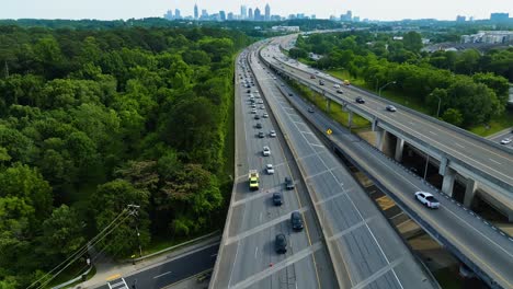 interstate highways with traffic in rural area. skyline silhouette with skyscraper in atlanta, georgia. aerial wide shot. traffic jam and green forest trees in summer