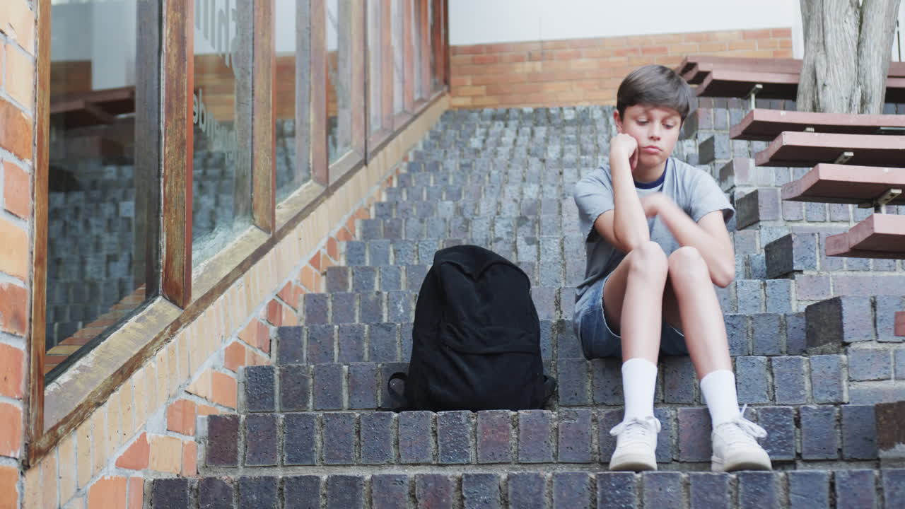 Sitting on school steps, boy looking sad with backpack beside him, copy space