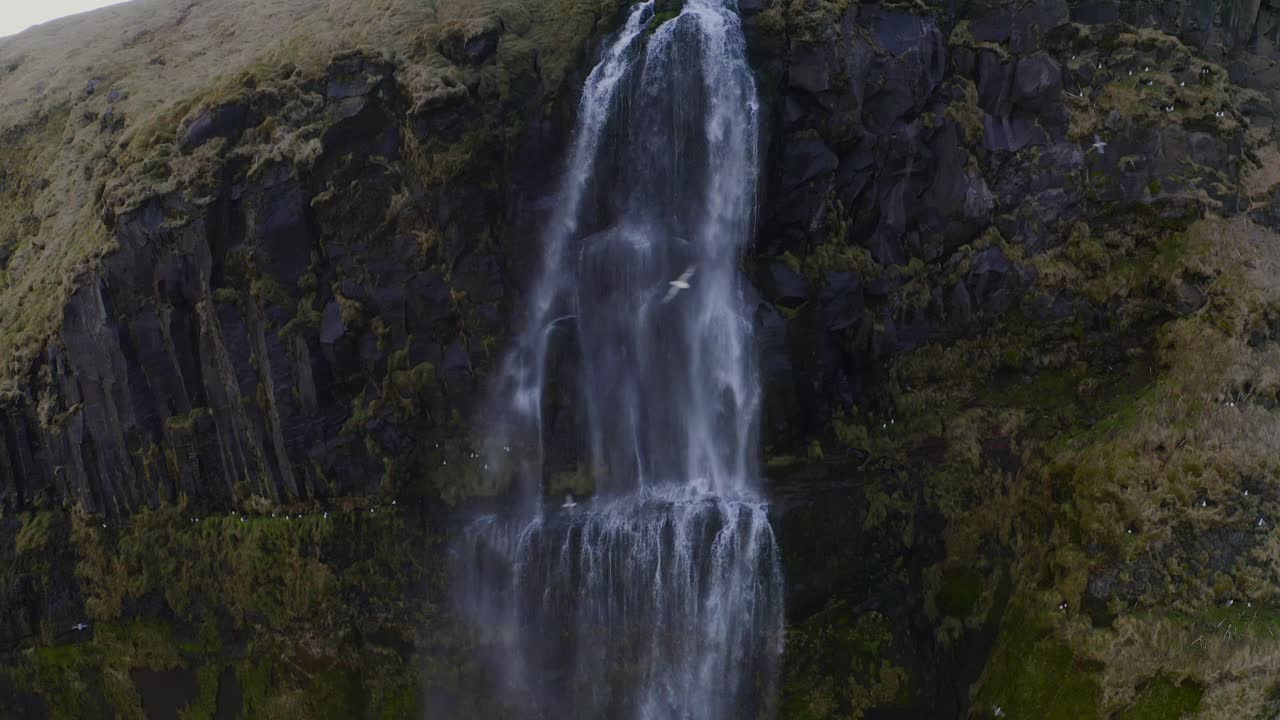 inclinándose hacia abajo desde la parte superior de una cascada alta donde el agua cae en picado por el borde hasta el suelo muy por debajo