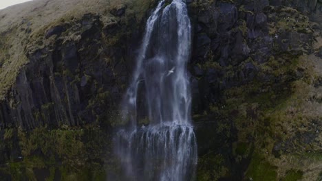 tilting down from the top of a tall waterfall where water is plummeting over the edge to the ground far below