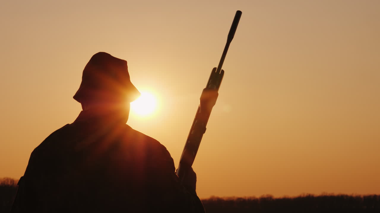 Un cazador con escopeta avanza por el campo hacia el sol poniente. Pasatiempo masculino.