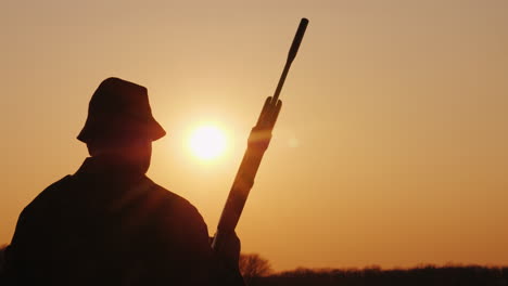 un cazador con un arma avanza por el campo hacia el sol poniente hobby para hombres steadicam sh