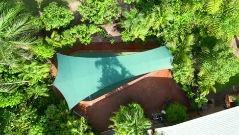 aerial drone of rural tropical estate exterior top down over pool with elegant green sun shade by home with solar panels