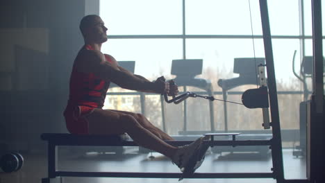 young man doing workouts on a back with power exercise machine in a gym club. at athletic man doing workouts on a back with power exercise machine in a gym on the background of large windows.