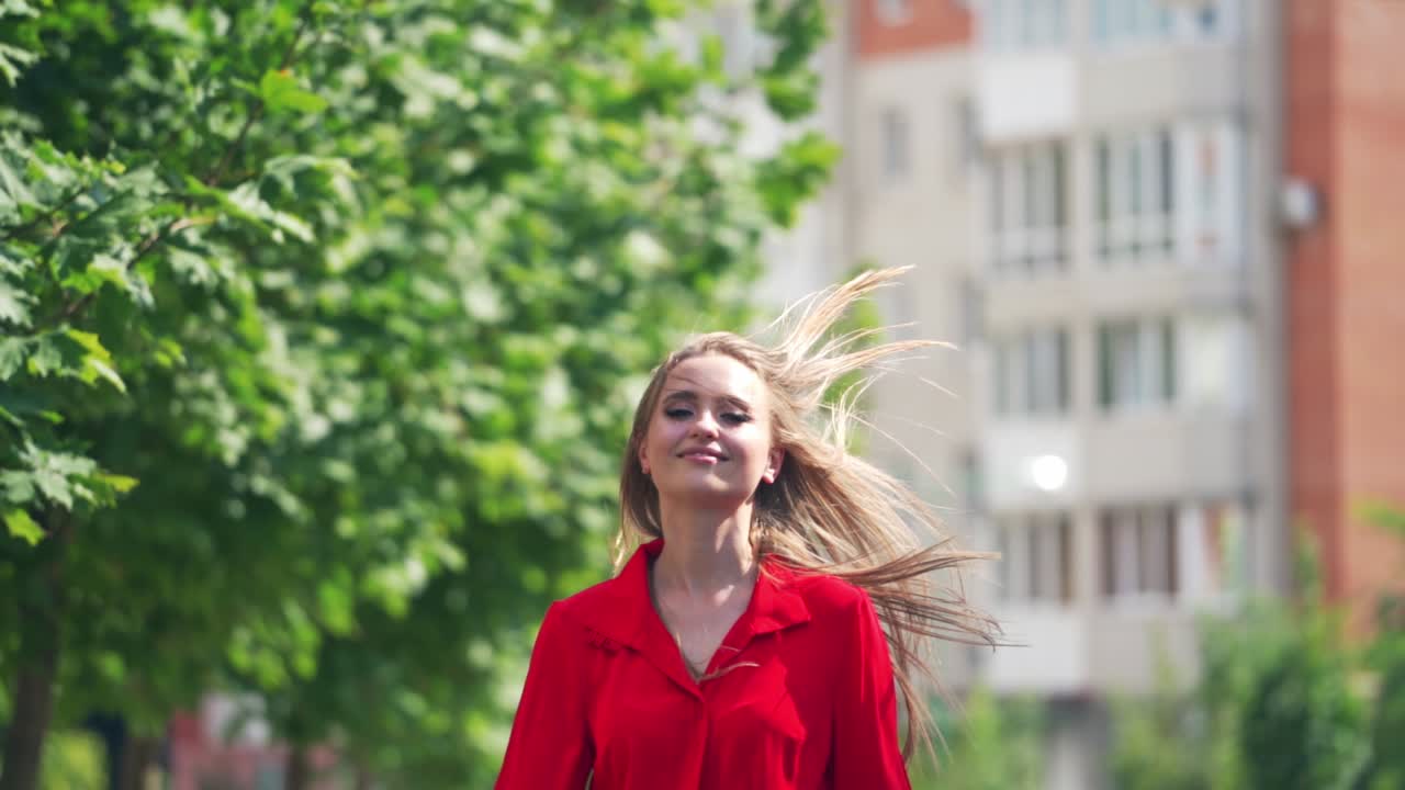 Front view of a smiling woman. Beautiful female in red passionate dress runs on the street in the city. Happy girl with long hair in move. Slow motion.