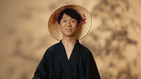 young asian man in black traditional costume and conus hat smiling cheerfully and giving a thumbs-up