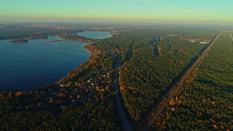 Aerial-birds-eye-shot-of-natural-blue-lake-surrounded-by-golden-trees-at-sunset-in-autumn