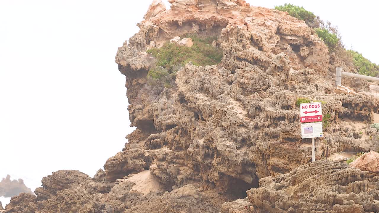 A rocky cliff with a warning sign, captured in natural daylight along Great Ocean Road, Australia
