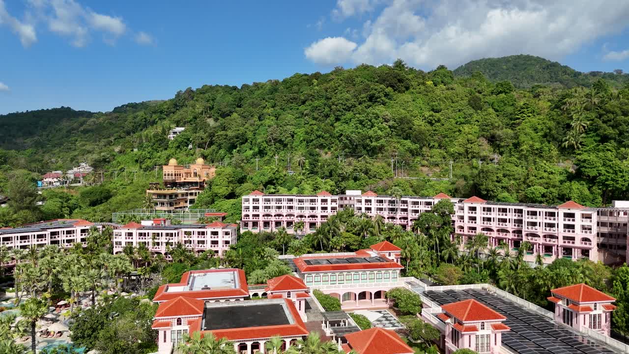 Aerial footage of a resort nestled in lush green hills under a bright blue sky in Phuket, Thailand