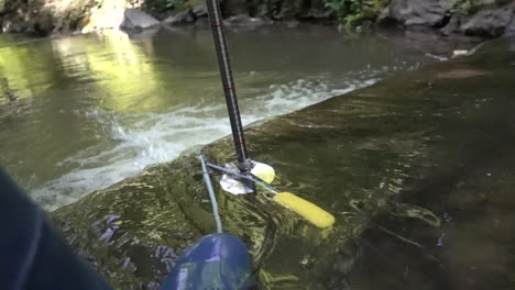 a scientist with boots tries to measure the flow of a river with a magnetic probe and a meter