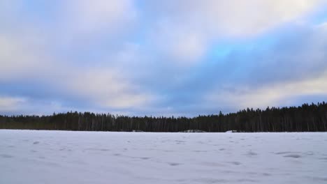 winter landscape at a frozen lake, forest, flying clouds in a blue sky