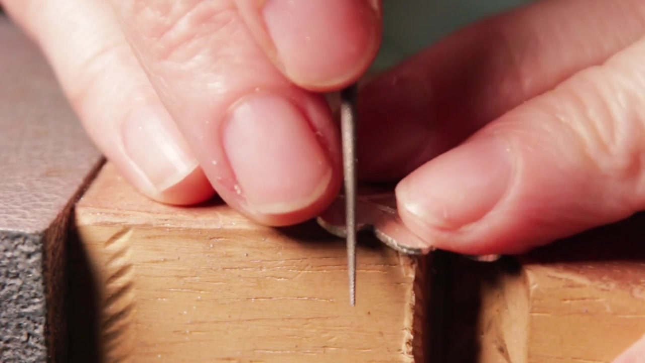Close-up of refining a silver leaf-shaped piece with a rounded file, smoothing edges and crevices on a bench peg. Ideal for jewelry making, craftsmanship, and metalwork content.