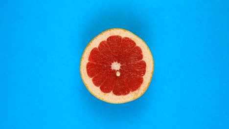 top view: half of an red grapefruit rotates on a blue surface - fast motion