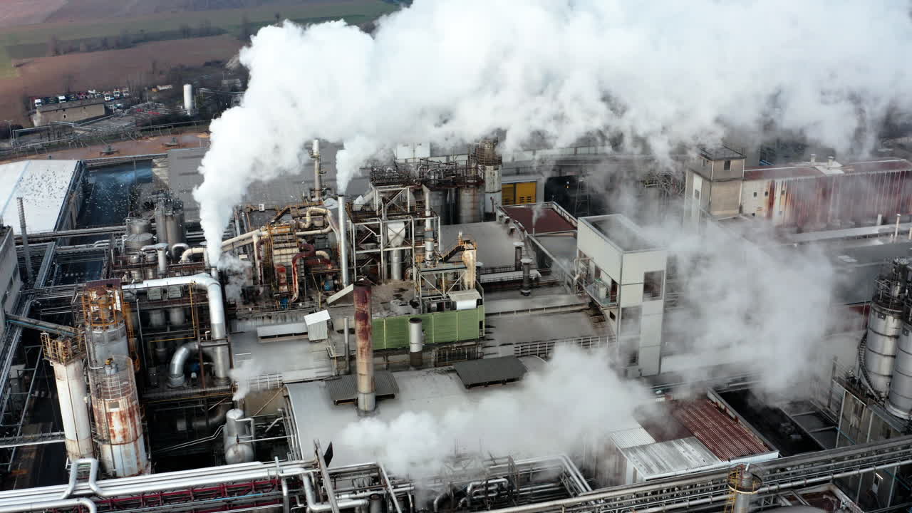 Dense industrial plant with large pipes and smoke billowing from chimneys