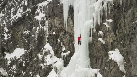 Spectacular-aerial-view-ice-climber-scaling-frozen-cascade-in-Maineline,-Kineo