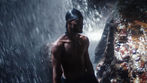 young black man stands under waterfall while travelling and exploring